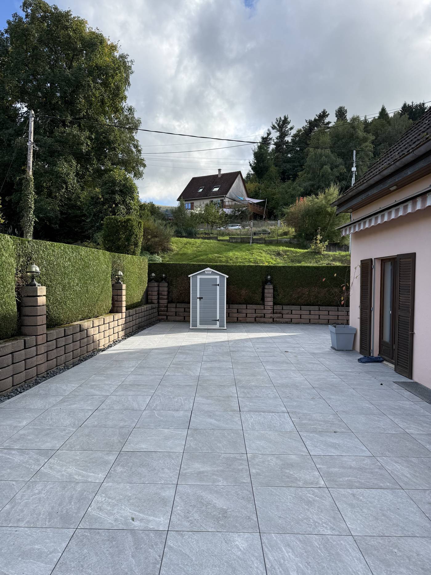 Cour dallée en grand format encadrée d’une haie taillée et d’un muret, réalisée par EK Paysage